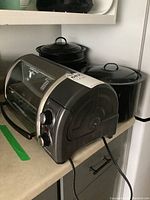 View of Hamilton Beach toaster oven on kitchen counter next to three black enamelware stock pots with lids.