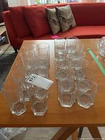 Overview of 22 hexagonal glasses on wooden table, 10 tall and 12 smaller glasses, some smaller with milky look