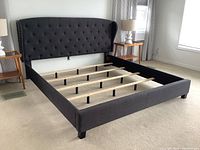 Full assembled view of grey fabric upholstered bed frame with headboard, rails, and slats in bedroom