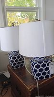 Two matching ceramic base lamps with blue and white patterned bases and white shades on a table near a window