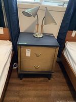 Nightstand next to beds with vintage dual head lamp standing on top, showing overall view of both items.
