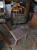 Photo showing full view of vintage men’s valet stand with wooden hanger, trouser ring, metal support rods, and cushioned seat in multicolored striped upholstery.