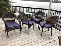 Four resin wicker patio chairs placed on a wooden deck with a lake view in the background, showing the full set and cushions.