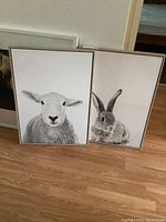 Front view of two canvas prints, one of a sheep and one of a rabbit, both with wood frames, leaning against a wall on a wooden floor.