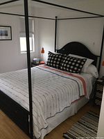 Full view of the black metal canopy bed frame with a mattress and bedding on it in a bedroom with a window and wall art.