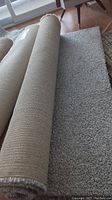 Rolled up light grey Ikea Alhede area rug showing the pile and backing material.