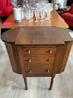 Front view of the solid wood sewing cabinet showing three drawers with wooden knobs, flat top surface and side compartments closed.