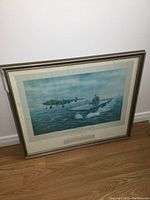 Framed print showing full view of military-themed artwork featuring airplane and aircraft carrier on the ocean.