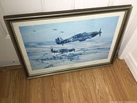 Framed print of WWII Spitfire planes titled 'Moral Support' placed on floor showing full framed piece.