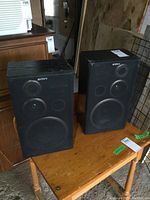 Pair of Sony black speakers placed on a wooden table, showing front and side view of both speakers.