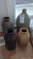 Four stoneware crocks and jug of varying sizes placed on wooden floor near a window, showing relative size and color variety.