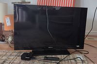 Full front view of Sony Bravia 32" TV with Apple TV box and remote placed in front.