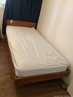 View of the twin bed from the head of the bed showing headboard and mattress covered by white sheet.