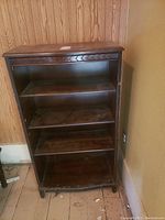 Antique wooden shelving unit against wall, showing four shelves inside and carved decorative edging on top