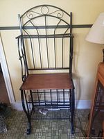 Front-facing photo of the metal and wood bakers rack with curved scrollwork top and wooden flat shelf.