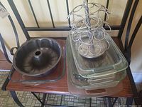 Set of Pyrex baking dishes, metal bundt cake pan, and metal spice rack on a wooden table with two chairs.