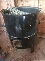Black metal barrel BBQ grill with cooking grate inside, showing exterior surface and legs.
