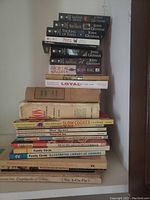 Stack of various cookbooks and novels including multiple by John Grisham and Brian Haig, older cookbooks with cloth covers and paperbacks with some wear.
