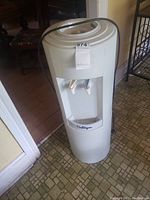 White Culligan water dispenser with two taps, plugged in and standing on a tiled floor.