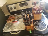Two wooden knife blocks with a variety of kitchen knives, mostly featuring black and reddish wooden handles, sitting on a stove.