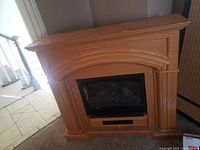 Front view of the electric fireplace insert in a wooden mantel, showing the carved wood surround and glass front panel.