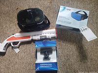 Photo showing black VR headset, boxed blue Onn VR headset, boxed PS3 Eye Camera, and white/orange toy gun