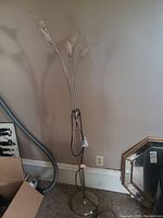 Full view of chrome floor lamp with five flexible arms and white glass shades against beige wall near outlet.