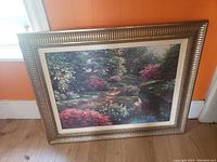 Front view of the large oil painting showing a garden scene with a stream and vibrant foliage in an ornate gold frame.