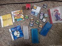 Photo of assortment of Nintendo DS game cartridges, cases, and small accessories laid on carpet floor.