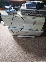 Two printers stacked; top is beige HP, bottom is white printer; multiple ink cartridges on top connected by cables