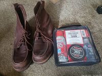 Pair of brown leather UGG boots alongside a transparent case shoe care kit with sprays and containers inside.