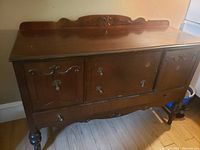 Front view of vintage wooden buffet cabinet with two side doors and central panel, showing carved wood detailing and metal handles.