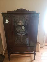 Front view of the vintage wood china cabinet showing the glass door with decorative wood grid and carved top and base.