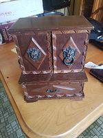 Closed view of the wooden jewelry box showing decorative lion head accents on front doors and bottom drawer