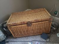 Exterior view of the rectangular wicker chest showing the natural woven wicker pattern, hinged lid, and metal latch closure.