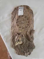 Front view of the wall clock featuring a sculpted wolf head and clock face on a wood-textured plaque.