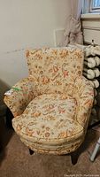 Front angled view of upholstered armchair showing floral fabric and wooden legs.