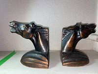 Pair of metal horse head bookends shown side by side from a side angle, displaying the sculpted horse heads and base shape.