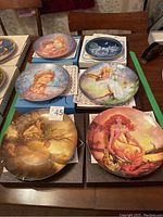 Photo showing six collector plates arranged on a table, artwork includes children, angels, and fantasy themes.
