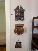 View of two wooden racks mounted on a wall with multiple collector spoons hanging and a wooden plaque with a metal decorative plate below them