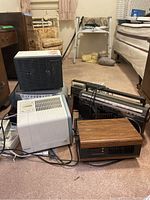 Overall lot of electronic appliances including heaters, air purifiers, boombox, and radio cassette player seen on carpeted floor with cords visible.