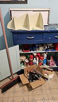 Full view of the bathroom cabinet shelf, blue cabinet with drawers, broom, and box of assorted tools and household items.