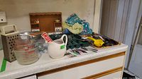 Photo showing Pyrex and Fire-King measuring cups, a box grater, white ceramic pitcher, and various utensils on a countertop.