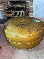 Full view of round yellow vinyl mid century ottoman with four legs near fireplace.