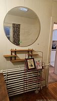 View of the round mirror mounted above the wooden wall shelf with the wire display rack positioned in front, showing wear and spots on mirror.