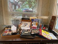 Full view of assortment of office supplies on a table including binders, portfolios, writing tools, lamp, and stamps.