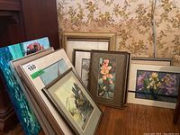 Overview photo showing seven framed paintings of varied sizes and styles leaning against a wall.