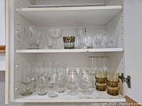 Cupboard shelf with variety of clear, amber, and gold trimmed glasses