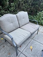 Photo showing front and side of outdoor love seat with light brown cushions and metal frame