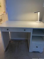 Full front view of white Restoration Hardware kids desk with central drawer and shelves on right side, lit by a white lamp on desktop.